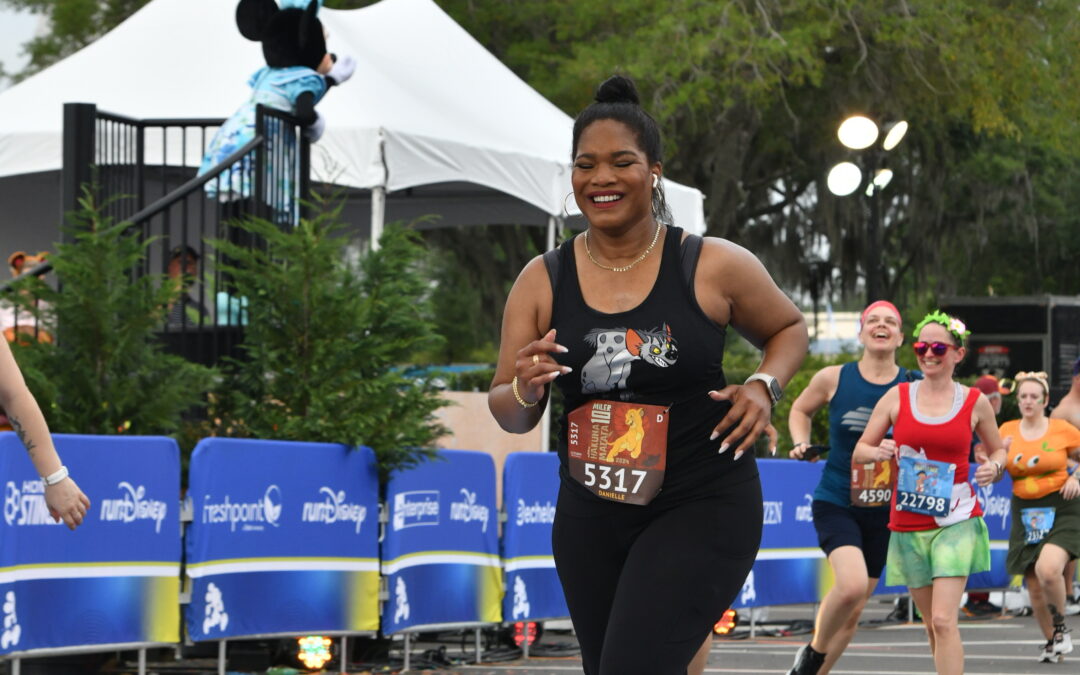 girl running in all black across the finish tree with Minnie Mouse in the background.